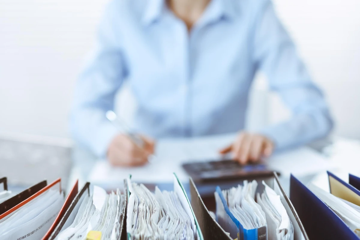 A woman at a desk with a calculator and folders, managing business tax records.