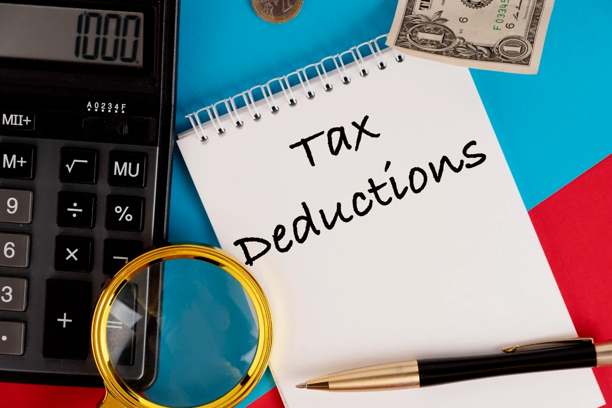 Tax deductions, the text is written in a white notepad, next to a calculator, a pen and a magnifying glass. 