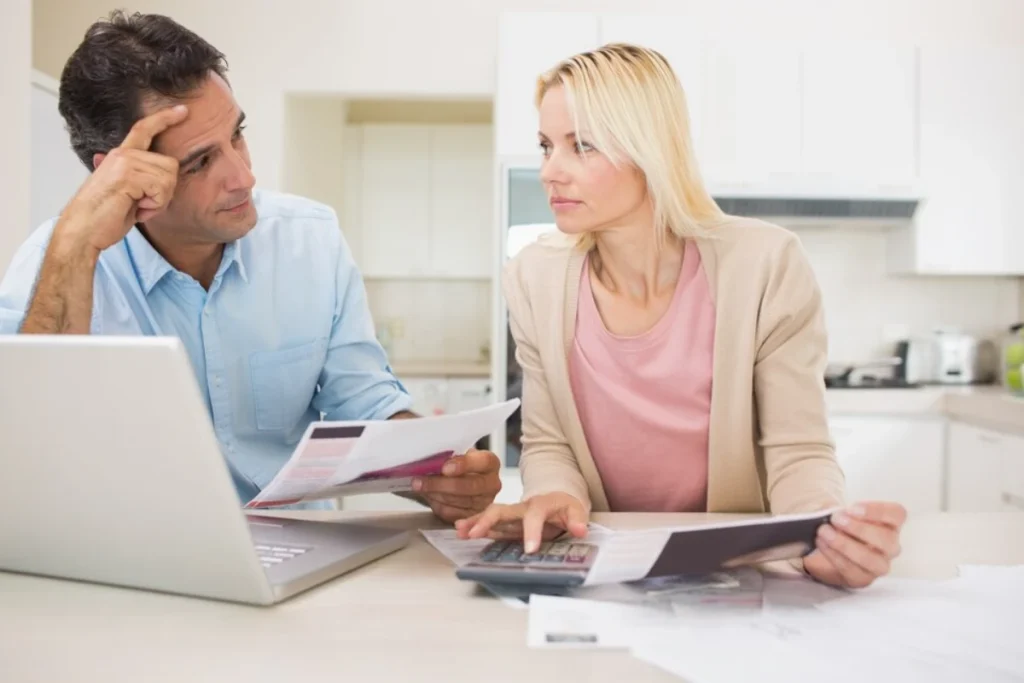 Worried couple with bills and a laptop in the kitchen talking about tax changes for new couples.