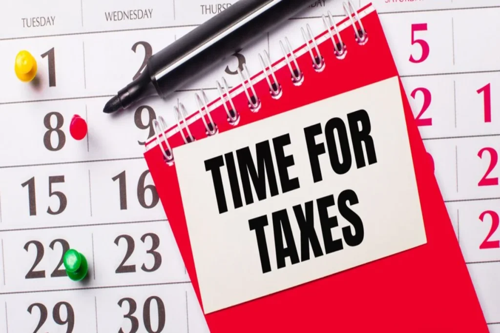 On the calendar is a white card with the text TIME FOR TAXES. Nearby is a red notepad and a marker. View from above
