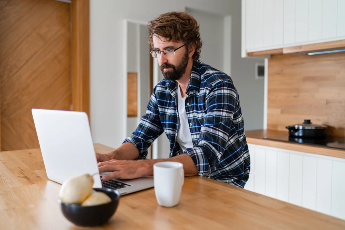 man-with-beard-plaid-shirt-using-laptop-kitchen